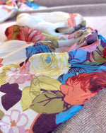 A close-up of a lightweight fabric with a colorful floral print, draped over a neutral textured surface.
